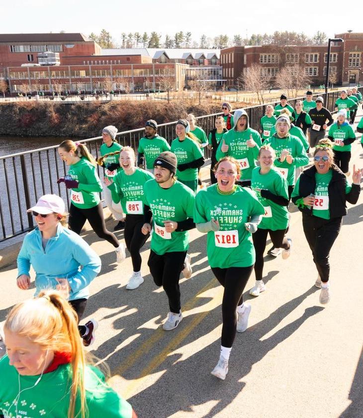 runners in green shirts crossing campus footbridge for a race 